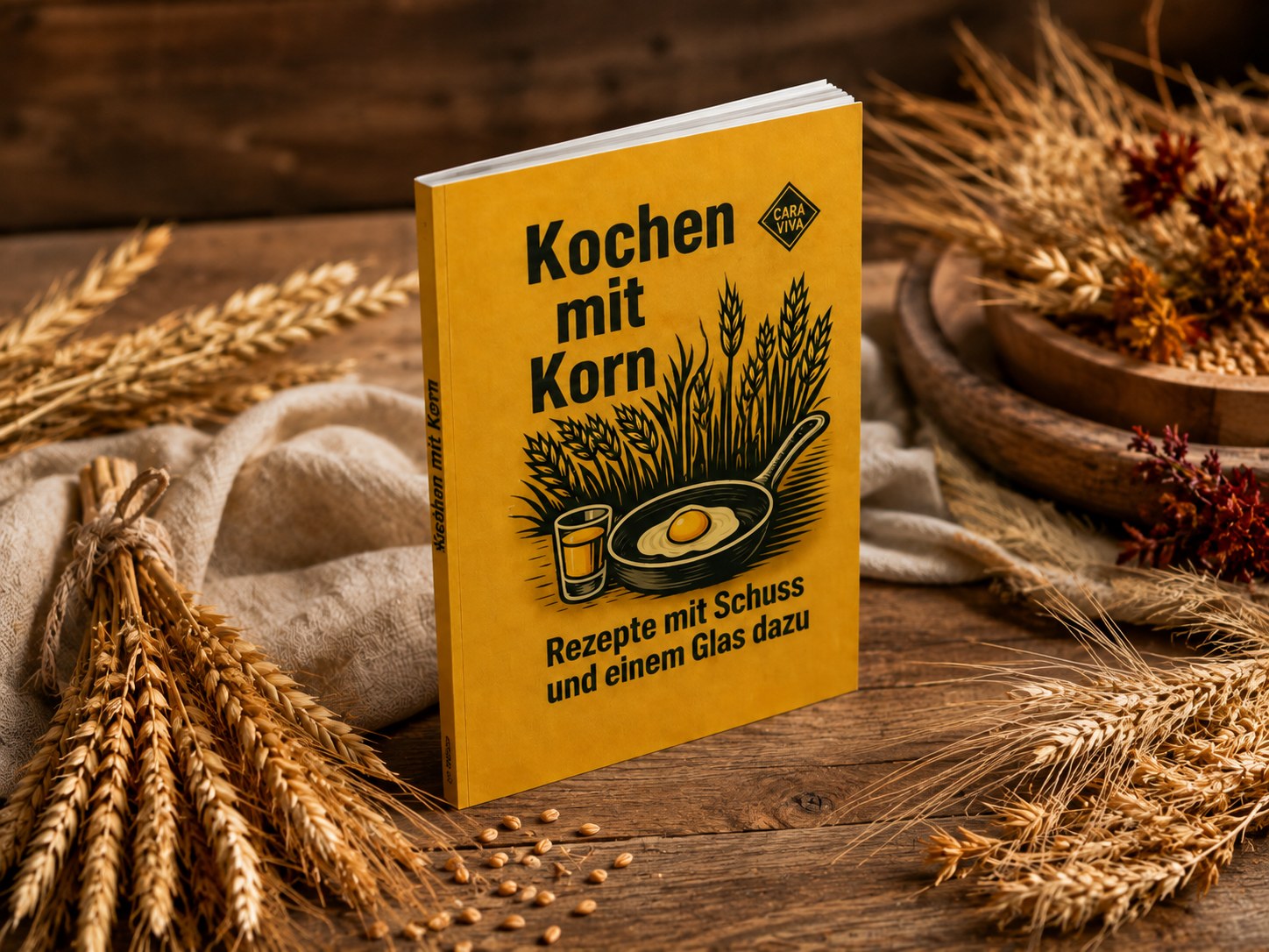 Kochen mit Korn auf einem Holztisch zwischen gebündelten Weizenähren, dahinter eine Holzschale mit Trockenblumen